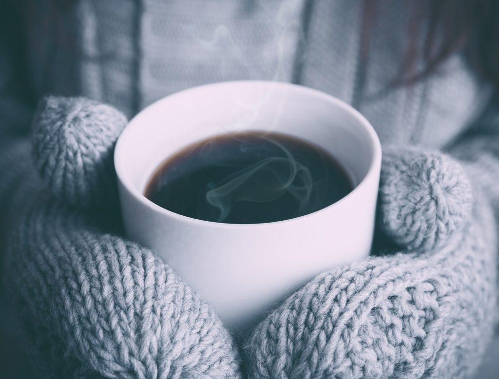 A pair of mittens holding a cup of coffee
